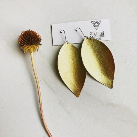 brass boho leaf earrings next to a wildflower against a marble background